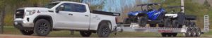 White pickup truck towing trailer with two ATVs