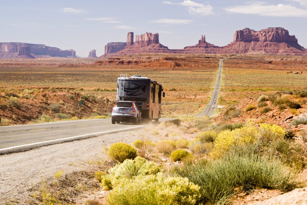 Recreational vehicle driving through Monument Valley with a flat tow vehicle