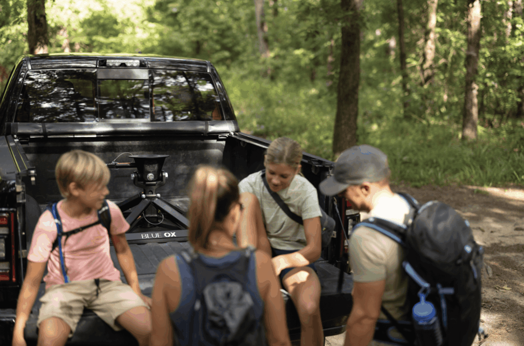 family sitting in truck bed with a blue of fifth wheel hitch attached